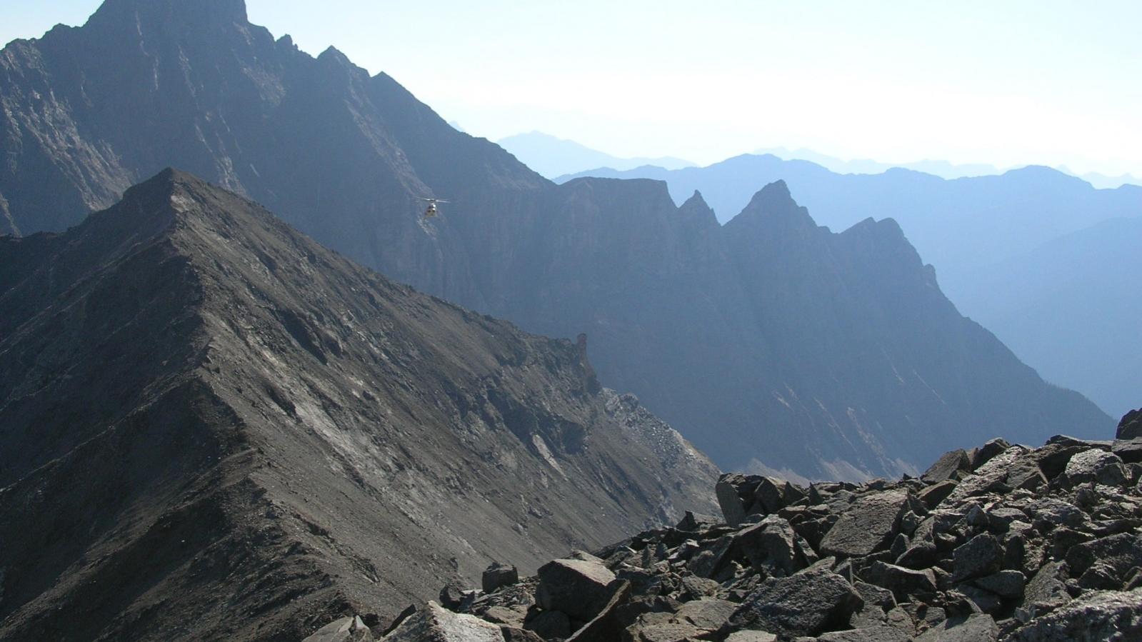Incoming helicopter - looking north at Butress Peak from ridge between REE Yippie and REE Base-Metal anomalies at the Ice River Complex Project Incoming helicopter - looking north at Butress Peak from ridge between REE Yippie and REE Base-Metal anomalies at the Ice River Complex Project
