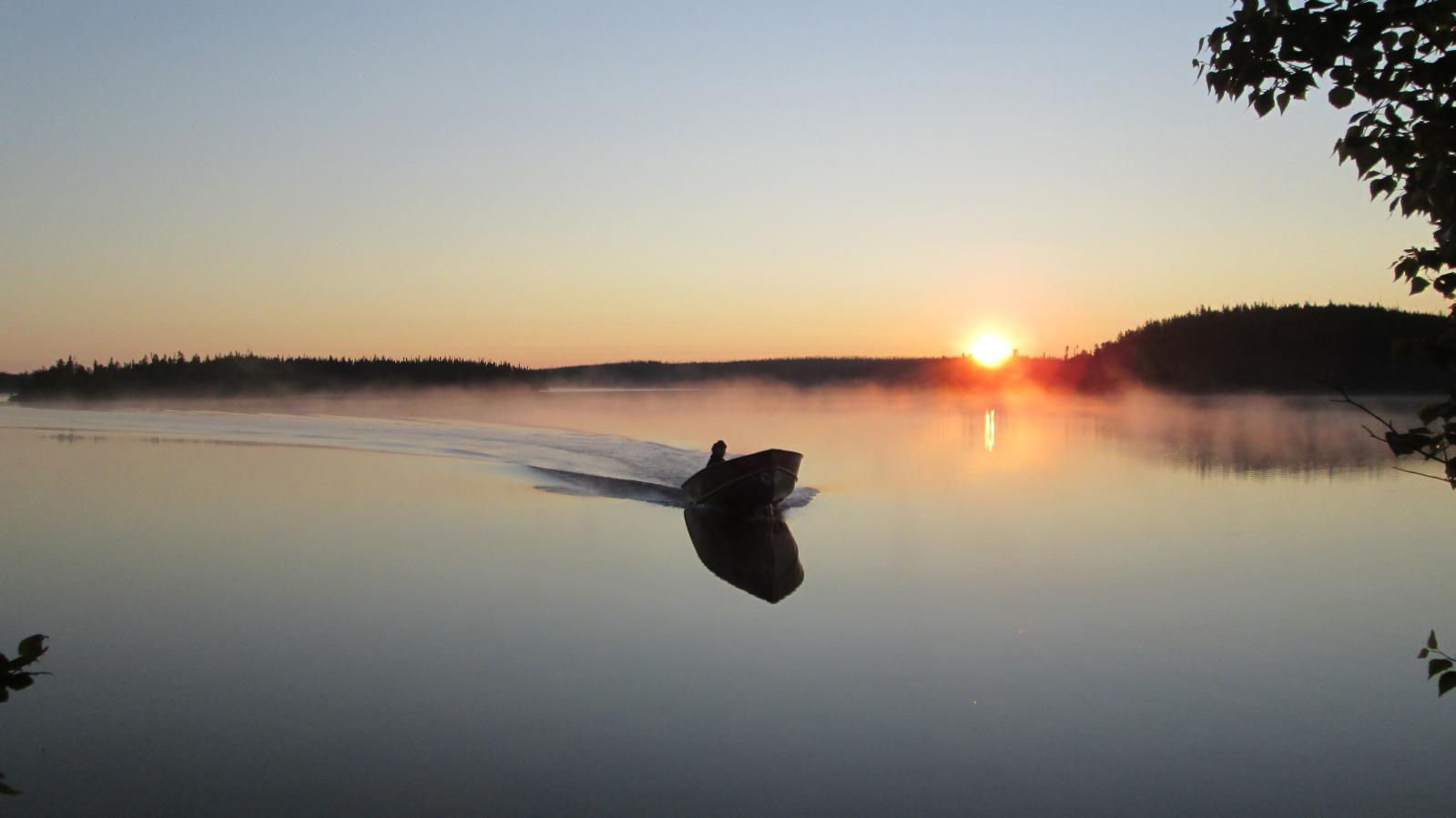 Motor boat on a placid lake with sunset A motor boat returning to camp on a placid lake near dusk with the sun setting in the background